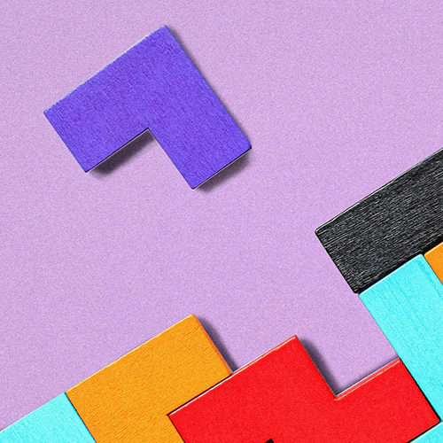 Colored wooden blocks on purple background with one piece about to fit in.